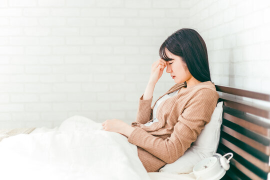 ベッドルームで眼精疲労や頭痛に悩む日本人女性
