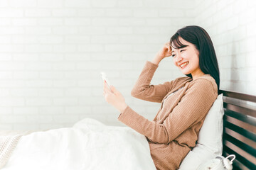 ベッドルームでスマホを見て照れる日本人女性
