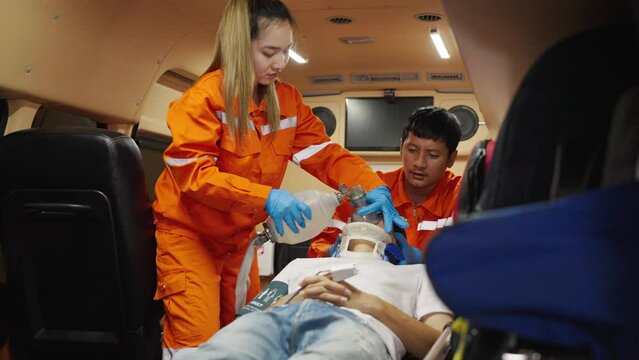 Asian emergency medical technician (EMT) or paramedic giving emergency oxygen with patient in ambulance car