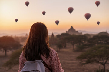 Young woman traveler enjoying with balloons over ancient pagoda at Bagan, Myanmar at sunrise - obrazy, fototapety, plakaty