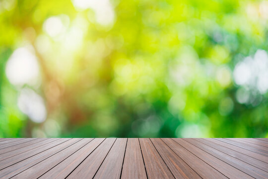Empty wooden terrace with abstract blurred image of green nature backgrounds with soft light