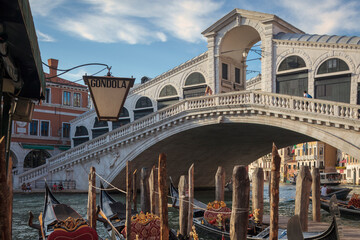 Venezia. Ponte di Rialto sul Canal Grande con pali e gondole in riva. - obrazy, fototapety, plakaty