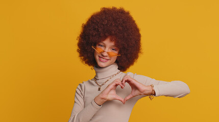 I love you. Smiling young teenager child girl kid makes heart gesture demonstrates love sign expresses good feelings and sympathy. Little funny children isolated alone on studio yellow background