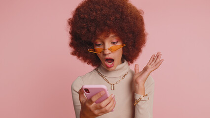 Young funny school girl in glasses use smartphone typing browsing, loses becoming surprised sudden...