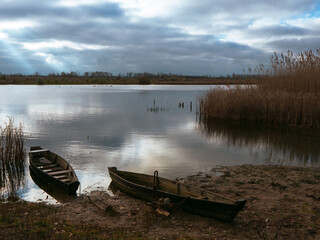 Obraz premium boats near the river bank at dawn. wooden boats on the water. clouds reflecting in the water of the river. canoe by the river.