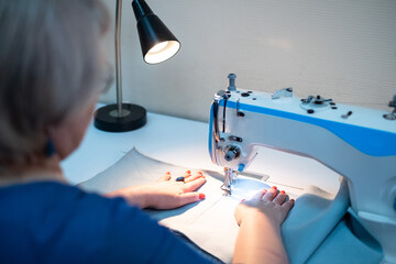 There is a professional sewing machine on the table, female hands hold the fabric and sew the product on the sewing machine.