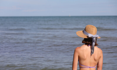 young girl back to back wears a wide straw hat to protect herself from the sun
