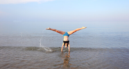 girl performs gymnastic exercises with her head upside down on the seashore in summer