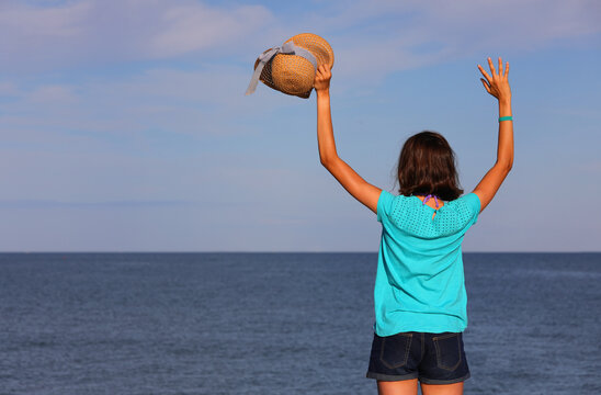 girl greets with straw hat towards the sea