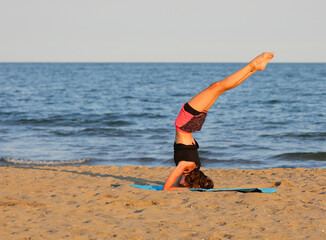 young slender girl does gymnastic exercises at the beach on the gym mat