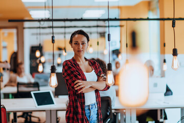 Fototapeta premium Female boss, manager executive posing in a modern startup office while being surrounded by her coworkers, team.