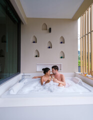 couple drinking champagne in a jacuzzi during honeymoon vacation, Asian Thai women and caucasian...