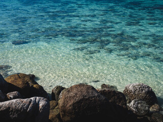 Scenic view of Sunset Beach, Koh Lipe Island. Rocky coastline against crystal clear turquoise sea with coral reef transparent shallow water. Satun, Thailand. Natural background with copy space.