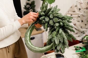 Woman decorates a Christmas wreath. Florist work concept before christmas holidays.