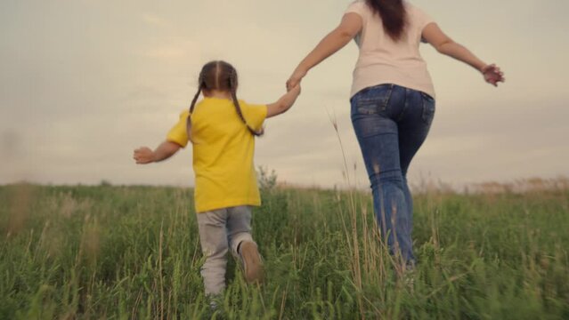 Happy family, child. Mom, little daughter run on green grass in meadow. Active family outdoor recreation, entertainment in park in nature. Mother, little girl play together outdoors, cheerful emotions