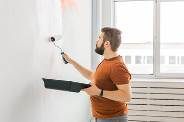 Man painting wall with paint roller - renovation and redecoration concept