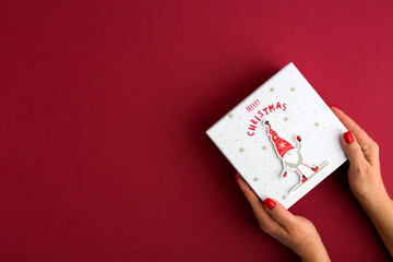 Female's hands holding gift box on red background. Christmas, New Year, Valentine's day and birthday concept.