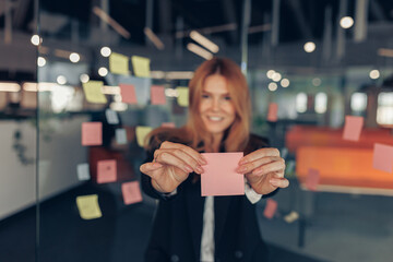 Businesswoman showing empty sticky notes while standing in modern office