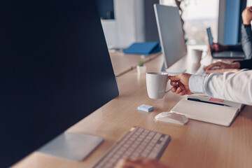 Businessman hands holding cup of coffee while sitting on his workplace in office