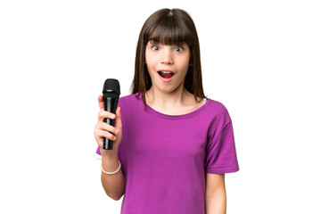 Little singer girl picking up a microphone over isolated background with surprise and shocked...