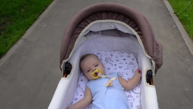 Baby boy is  riding in a stroller while walking.