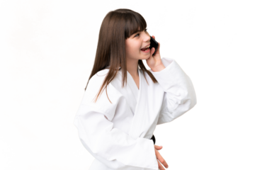 Little Caucasian girl doing karate over isolated background keeping a conversation with the mobile phone