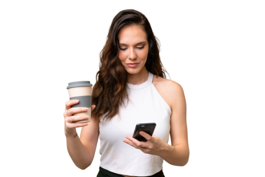 Young caucasian woman isolated over isolated background holding coffee to take away and a mobile