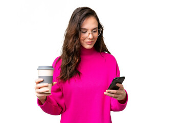 Young caucasian woman isolated over isolated background holding coffee to take away and a mobile