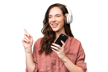 Young caucasian woman over isolated background listening music with a mobile and singing