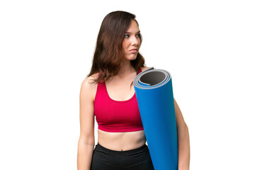 Young sport woman going to yoga classes while holding a mat over isolated background looking to the...