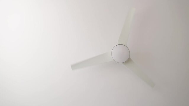 Isolated rotating white ceiling fan with light turned off from below, slow motion