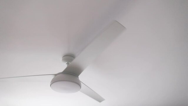 Isolated rotating white ceiling fan with light turned off, slow motion