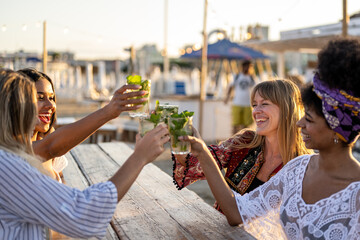 Happy young women wearing bikinies and beach wear and drinking cocktails on a tropical beach during vacation, people luxury travel, women toasting on holiday