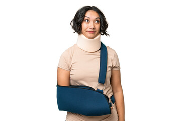 Young argentinian woman wearing neck brace and sling over isolated background and looking up