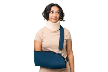 Young argentinian woman wearing neck brace and sling over isolated background and looking up