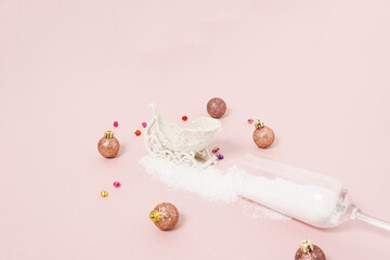 Champagne glass with snow decorated with baubles and sleigh bright pastel pink background. Christmas or New Year party concept. Minimal winter holiday season idea with copy space.