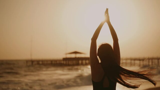 Sun Salutation. A young woman does Surya Namaskar at sunset. The girl raises her hands in greeting to the sun