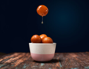 Gulab Jamun served in a bowl with pouring sweet syrup.