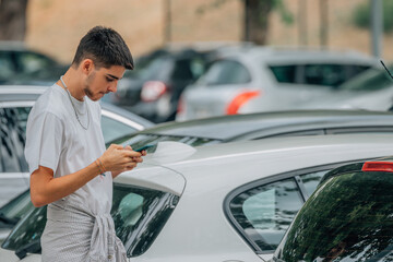 young man with mobile phone between cars