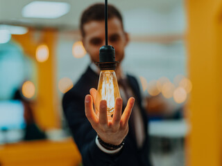 Symbolic photo of a businessman holding a light bulb in his hand in a modern office