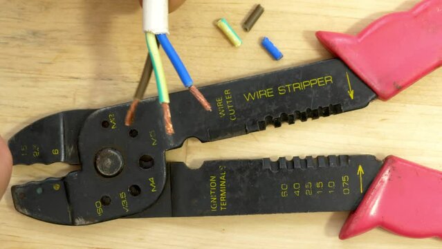 Closeup overhead shot of a man&rsquo;s hand preparing newly trimmed blue, brown and green cable wires, near a wire cutter tool, ready to add a UK electrical plug.