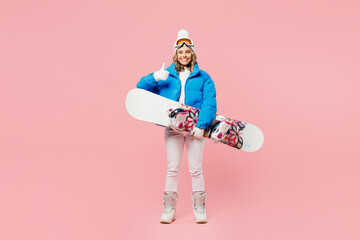 Full body snowboarder woman wear blue suit goggles mask hat ski padded jacket snowboard show thumb up isolated on plain pastel pink background. Winter extreme sport hobby weekend trip relax concept.