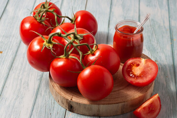Delicious red ripe tomatoes on a wooden board and a jar of their traditional sauce.