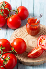 Delicious red ripe tomatoes on a wooden board and a jar of their traditional sauce.