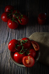 Delicious red ripe tomatoes on a wooden board and a jar of their traditional sauce. Dark food