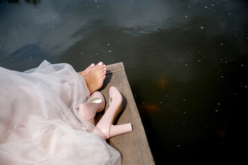 shoes and bare feet of the bride on a wooden deck against the background of water