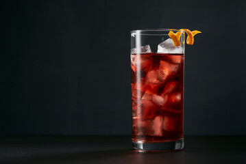 Negroni cocktail in highball or collins glass with orange peel on a dark background.