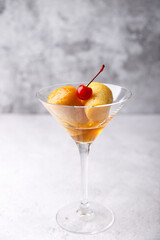 Neapolitan Rum baba (or baba au rum) in a martini glass with a cocktail cherry on a gray background. Small yeast cakes soaked in rum syrup. Traditional Italian pastry. Close-up, selective focus.