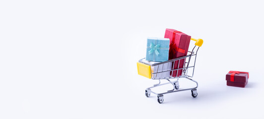 Miniature cart with gifts on a white background. Holidays shopping concept. Holidays New Year, Christmas, birthday. Copy space. Selective focus, close-up.