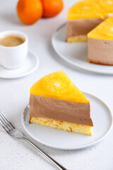 Chocolate-orange mousse cake with biscuit base, jelly and orange circles. Piece of homemade cheesecake and a cup of coffee. Traditional holiday dessert. Selective focus, close-up.